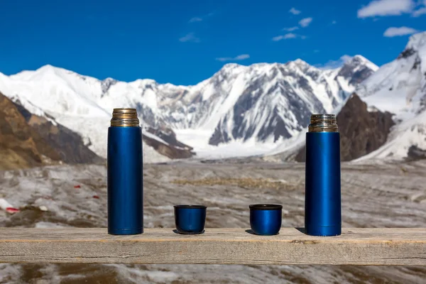 stock image Two Blue Thermoses and Cups on Wooden Table with Beautiful Himalaya Mountains on Background