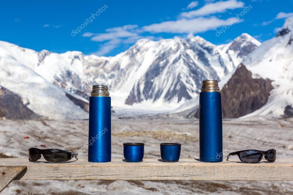 Two Blue Travel Thermoses Cups and Sunglasses on Wood Table and Mountain Landscape