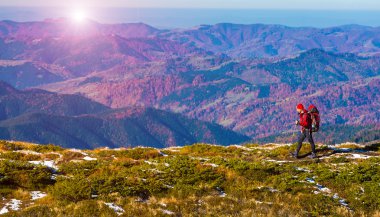 Hiker walking on Mountain Ridge with Backpack Autumnal Landscape and Sun