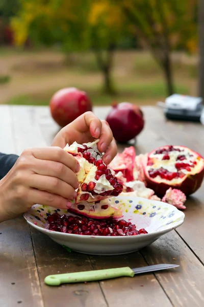 Female Hands cleaning fresh pomegranate on wooden table — Stock Photo, Image