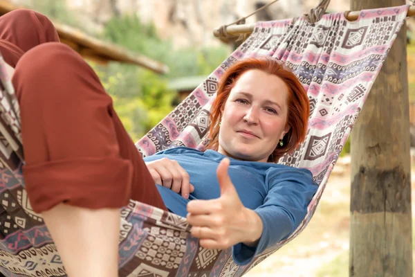 Žena leží v houpací síti na terase venkovských dřevěnice s Ok gesto — Stock fotografie