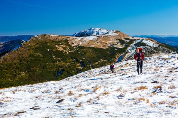 Два человека поднимаются по снежному склону с видом на горы — стоковое фото