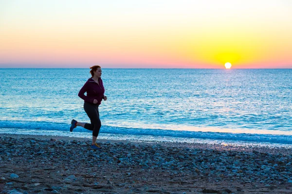 Junge Frau joggt am Strand entlang der Brandung bei Sonnenaufgang — Stockfoto