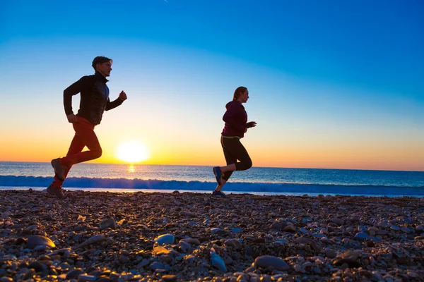 Sportif çift sabah koşu deniz plajda güneş doğarken yapıyor — Stok fotoğraf