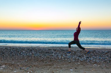 Genç kadının yoga egzersiz tropik sahilde güneş doğarken yapması