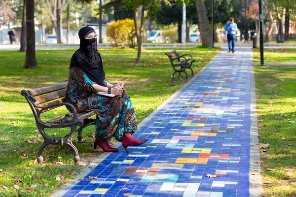 Восточная женщина сидит на скамейке в красочной аллее парка — стоковое фото