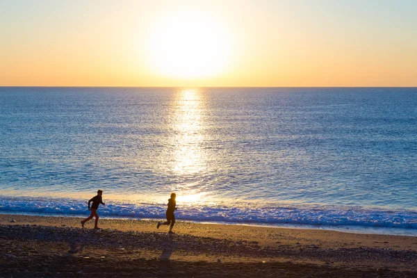 日の出の海のビーチでジョギングを行うスポーティなカップル — ストック写真