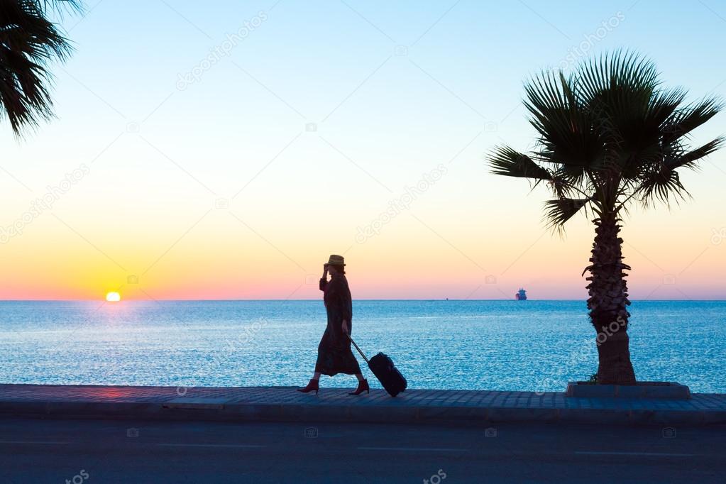 Exotic Vacation Silhouette of Female pulling Travel Suitcase on Seafront