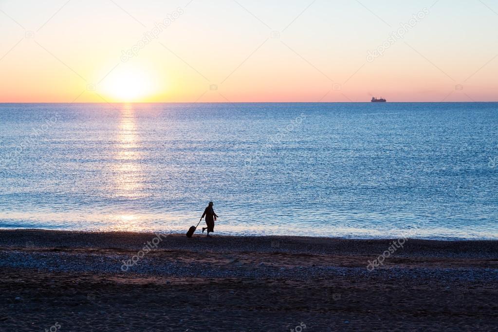 Exotic Vacation Silhouette of Female pulling Travel Suitcase along Ocean Beach