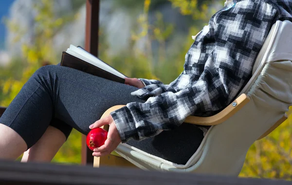 Som sitter i stol inne i lantlig trädgård läser bok hålla granatäpple — Stockfoto