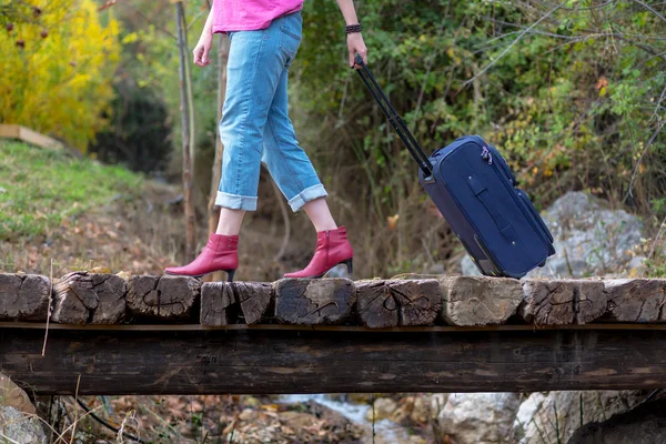 Persona che cammina sul vecchio ponte di legno tirando valigia da viaggio — Foto Stock