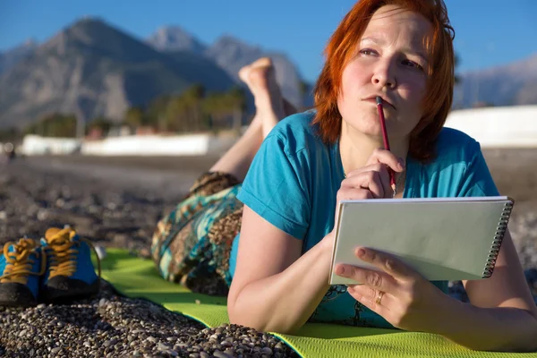 Vrouw liggend op de Mat met schetsboek en potlood nadenkend zoeken — Stockfoto