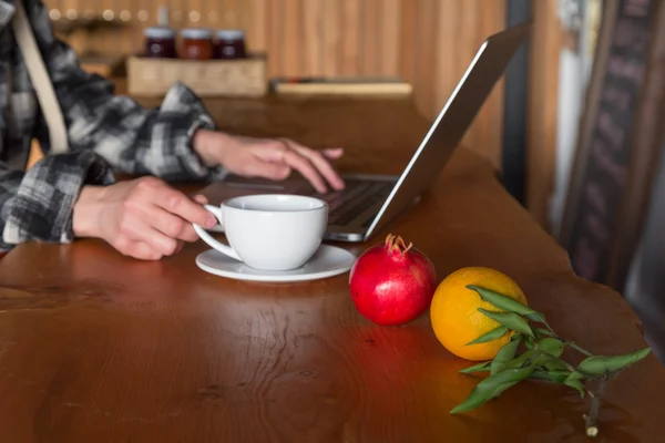 Persona che lavora al computer al tavolo di legno con frutta in primo piano — Foto Stock