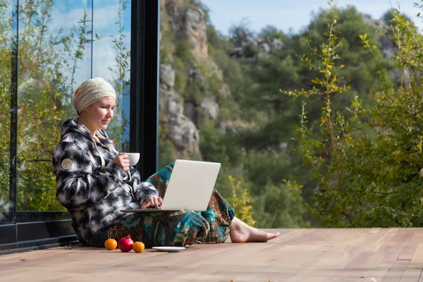 Leuke vrouw zitten op het terras van houten cabine met Laptop en koffie — Stockfoto