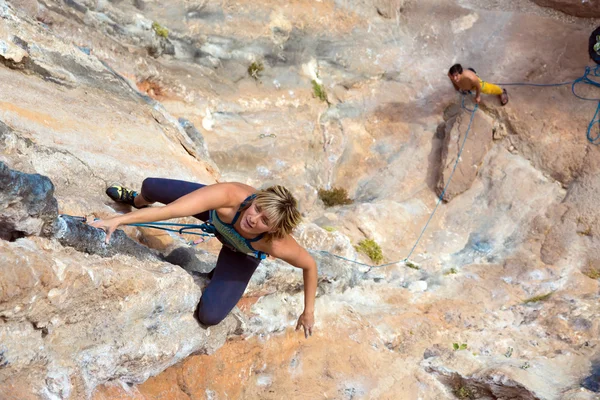 Woman Climber hanging on vertical Rocky Wall her Partner bleating and watching up