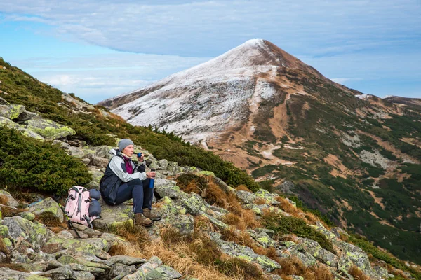 Escursionista femminile seduta sulla pietra verde con vista panoramica sulle montagne — Foto Stock