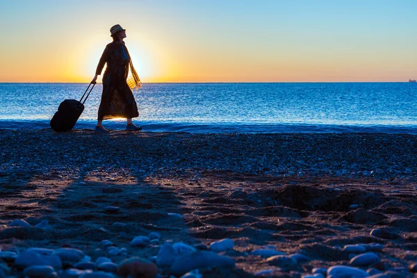 Silhouette einer Dame, die an der Brandung entlang läuft und Reisekoffer zieht — Stockfoto