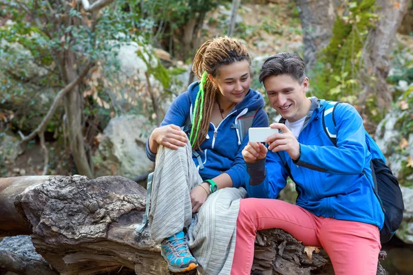 Hombre y chica sentados en el bosque y mirando la pantalla del teléfono — Foto de Stock