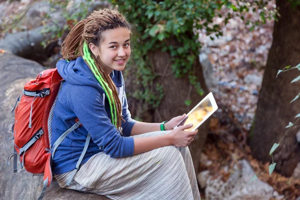 Gülümseyen ve beyaz Tablet tutan ormanda oturan sevimli kız — Stok fotoğraf