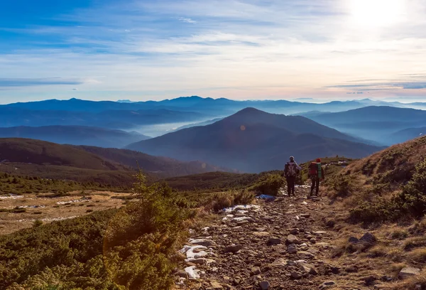 Dağ yolu günbatımı Dağları arka planda yürüyen iki yürüyüşçü — Stok fotoğraf