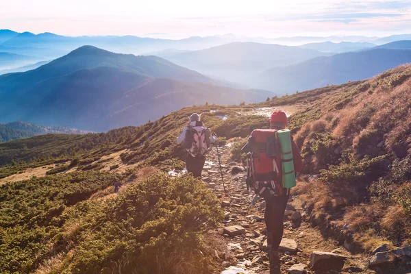 Twee wandelaars lopen op berg pad zonsondergang bergen achtergrond — Stockfoto