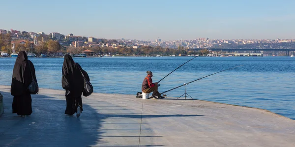 Pescador sentado en el paseo marítimo y musulmán vestido Damas caminando — Foto de Stock