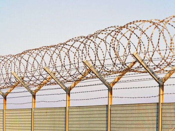 Detail of a metal grid fence with loops of  Concertina razor wire and barbed wire