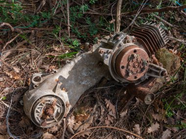 Ormanda terk edilmiş bir scooter 'ın hurda motoru ve şanzımanı, doğal çevrenin bozulma ve kirlenmesinin sembolü.