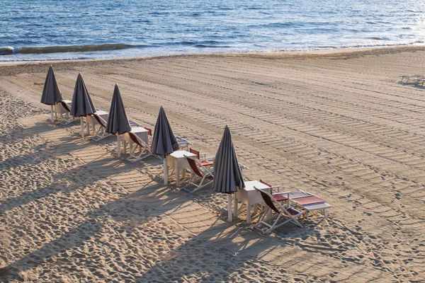 Line of closed beach umbrellas loungers, chairs and sunbeds — Stockfoto