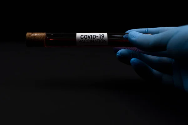 Les mains fermées et gantées tiennent le produit chimique dans une fiole étiquetée covide-19. Analyse chimique en laboratoire et concept de vaccin contre le coronavirus. — Photo