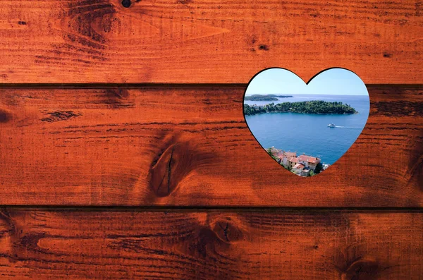 Hjärtformade hål med blå havet, grön ö och kuststad i en brun trävägg. — Stockfoto