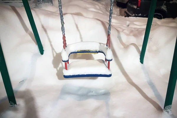 Snow-covered swing on the playground in the yard