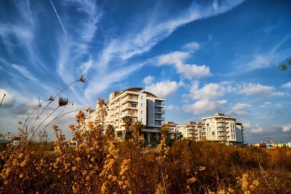 Modern big building, tree and greenery on foreground and blue sky on background. Hotel of block of flats is surrounded by green trees in summer. The concept of nice summer day in Turkey