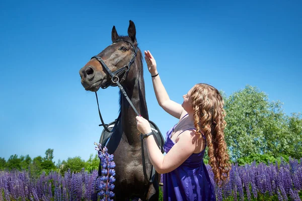 Fat girl with long curly hair with brown horse outdoors on a Sunny day