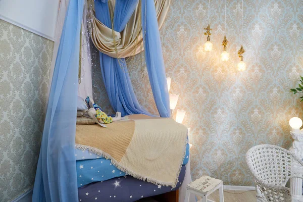 Bed in a room with a blue canopy and a yellow bedspread. Beautiful lamps on the wall. Photo studio for photography