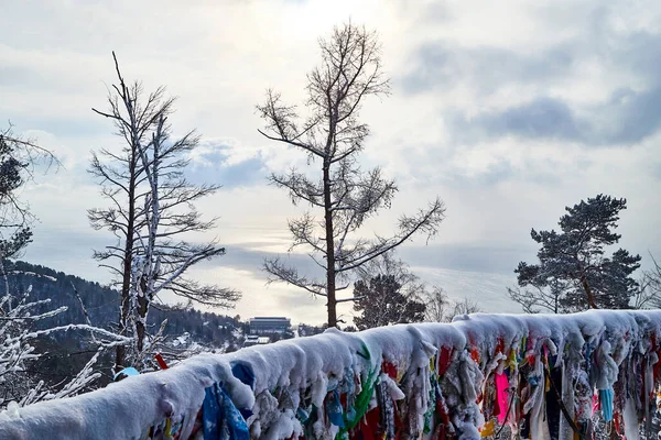 Buddhist multicolored wish ribbons at a height in the mountains above Lake Baikal in Russia. High landscape with Fencing with colored ribbons on cliff with trees