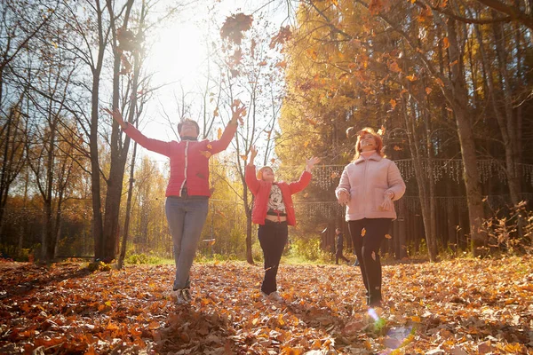 Two middle aged women and young girl in autumn park with yellow leaves. Mother and daughter on a walk. Aunt and niece outdoors