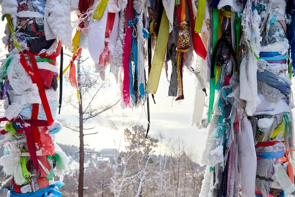 Buddhist multicolored wish ribbons at a height in the mountains above Lake Baikal in Russia. High landscape with Fencing with colored ribbons on cliff with trees