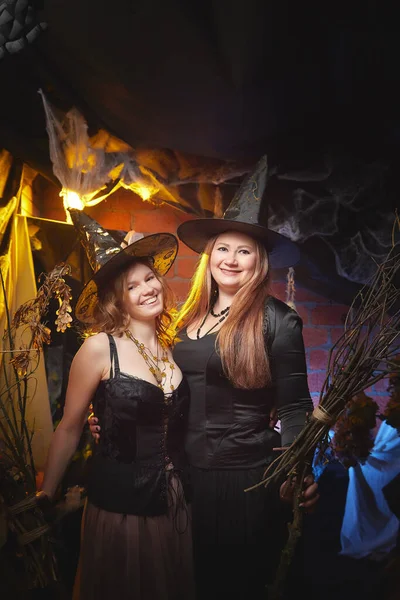 Two young women looking like witches are having fun on Halloween in a dark room with yellow light and smoke. Carnival concept and Halloween party