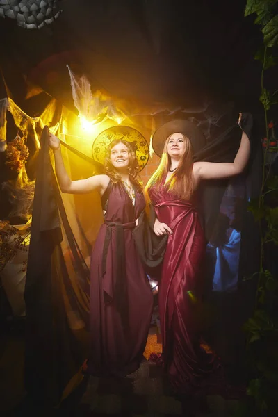 Two young women looking like witches are having fun on Halloween in a dark room with yellow light and smoke. Carnival concept and Halloween party