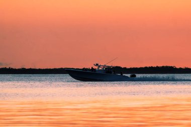 Altın Saat Navigasyonu: Orta Konsol Balıkçı Teknesi Canlı Anahtar Günbatımına Karşı Siluet
