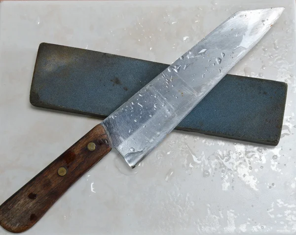 Cuchillo y piedra de afilar en el suelo de baldosas — Foto de Stock