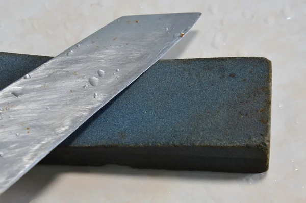 Cuchillo de cocina y piedra de afilar en el suelo de baldosas — Foto de Stock