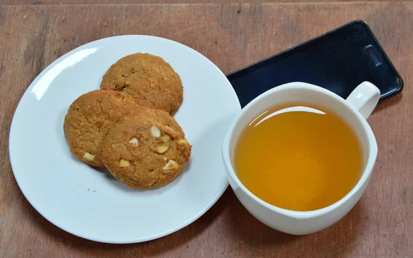 Galleta de cacahuete y taza de té con teléfono móvil negro — Foto de Stock