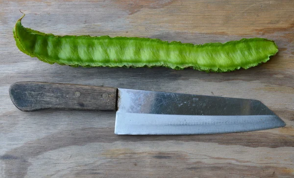 Feijão de asa longa e faca de cozinha na placa de madeira — Fotografia de Stock
