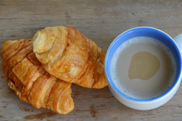 Croissant e café com leite em tábua de madeira — Fotografia de Stock