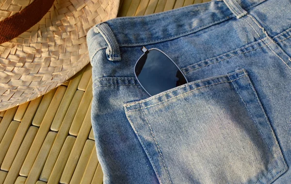 Kacamata hitam di saku belakang jean biru dan topi bambu di hari yang cerah — Stok Foto