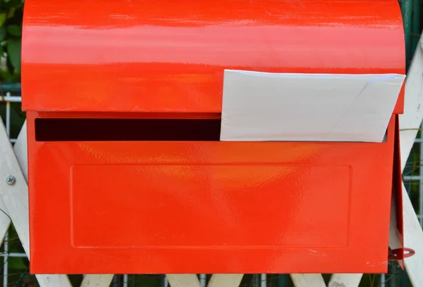 Білий конверт в червоній поштовій коробці на домашньому паркані — стокове фото