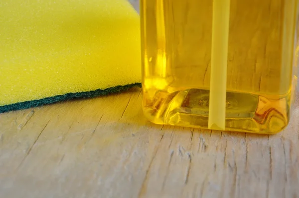 Sárga edénymosogató szappan és cserjések szivacs, fából készült táblán — Stock Fotó