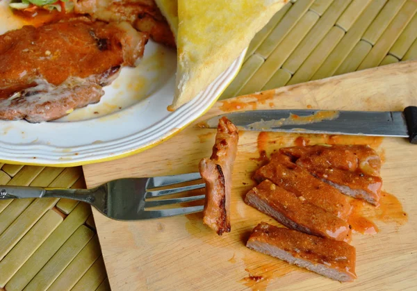 Steak babi panggang yang dipotong di atas piring pemotong kayu. — Stok Foto